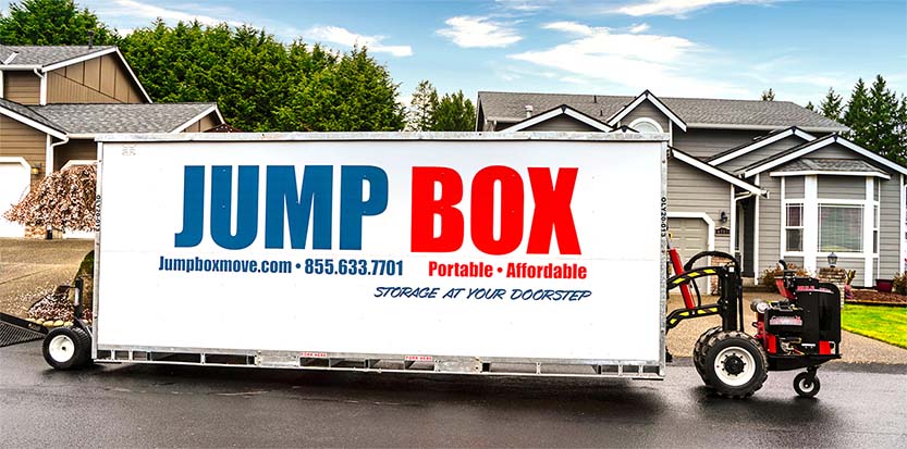 A portable storage container with a Jump Box Mobile Storage logo on the side, in front of a house. Jump Box Mobile Storage offers portable storage containers in Tacoma and Olympia.