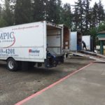 An open commercial moving truck is parked in front of an office, belonging to Federal Way movers, Olympic Moving and Storage.