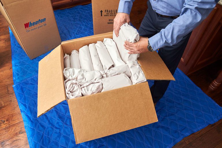 An Olympia moving company packing service employee wrapping dishes in paper and carefully placing them in a moving box.