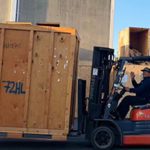 A Tacoma Moving Company mover, offering short & long-term storage by operating a forklift, moving a large wooden crate, on a street, near a secure storage solution. Storage near me.