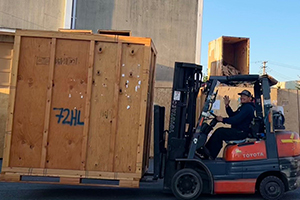 A Tacoma Moving Company mover, offering short & long-term storage by operating a forklift, moving a large wooden crate, on a street, near a secure storage solution. Storage near me.