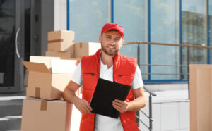 A Washington mover in a vest holds a clipboard, in front of moving boxes, representing the 5 must-haves in a moving company.