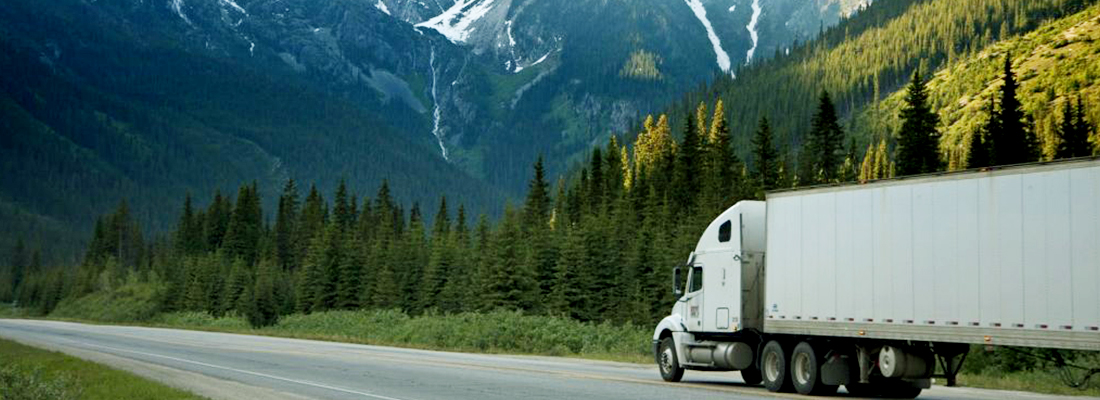 A moving truck driving down a Washington mountain road, surrounded by breathtaking scenery, represents the pros and cons of moving to the mountains.