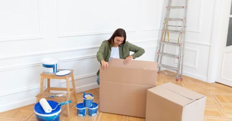 A woman holding open and looking into a moving box in a room, demonstrating the best packing tips for your 2023 move by packers and movers.