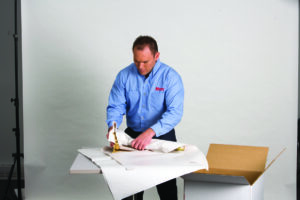 An interstate and long distance mover professionally packing a fragile object, in paper, on a table.