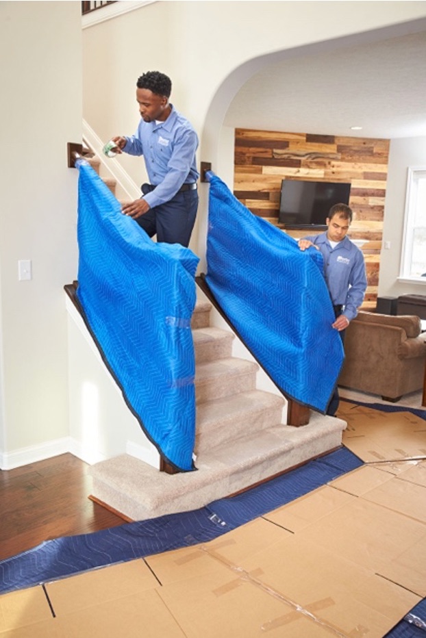 Local movers in blue shirts and pants cover the stairs' handrails with blue moving blankets.